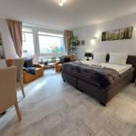 Ein Schlafzimmer mit Bett, Sessel und großem Fenster. Holzfußboden und Wandbild.