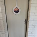 Eingangstür mit Dekorationskranz und Metallgriff zwischen weißen Ziegelwänden.