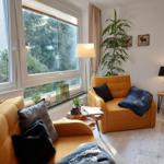 Wohnzimmer mit gelben Sitzmöbeln, großen Fenstern und Zimmerpflanzen.