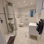 Badezimmer mit Dusche, WC und Waschbecken. Weiße Fliesen und moderne Einrichtung.