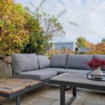 Terrasse mit grauem Sofa, Holztisch und Pflanzen im Hintergrund.