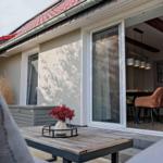 Terrasse mit Tisch und Blumen. Durch Glastür ist Esszimmer sichtbar.