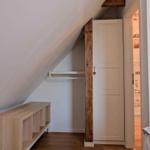 Schlafzimmer mit Dachschrägen, Kleiderschrank und Holzregal.
