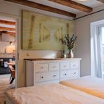 Schlafzimmer mit Blick auf Garten, weiße Kommode und Küchenbereich im Hintergrund.