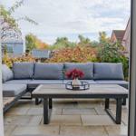 Terrasse mit grauem Sofa und Holztisch. Im Hintergrund sind Bäume und Sträucher zu sehen.