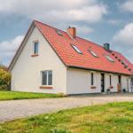 Ein Haus mit rotem Dach und weißen Wänden. Vor dem Haus liegt ein gepflasterter Weg.