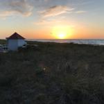 Sonnenuntergang am Strand mit kleinem weißen Gebäude und rotem Dach.