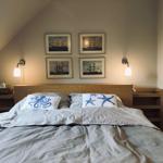 Schlafzimmer mit Bett, Wandbildern und Nachttischen unter Dachschrägen.