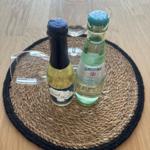 Zwei Getränkeflaschen und ein Weinglas auf einem runden Tischset.