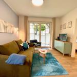 Wohnzimmer mit Sofa, Couchtisch und Fernseher. Durchgang zur Schlafzimmer.
