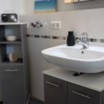 Waschbecken mit Spiegelschrank und kleinem Regal an der Wand.