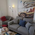 Wohnzimmer mit grauem Sofa, Kissen und Wandbild mit Oldtimer. 