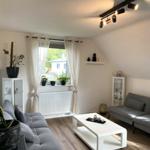 Wohnzimmer mit grauem Sofa, weißem Tisch und Pflanzen an Fenster.