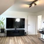 Wohnzimmer mit Fernseher, Pflanzen und Holzboden. Tür führt in andere Räume.