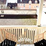 Balkon mit zwei Stühlen und Tisch, Blick auf Dächer und Steinmauer.