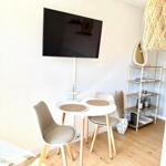 Runde Esstisch mit Stühlen, Wandfernseher und Regal im Raum.