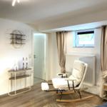 Ein Raum mit weißem Schaukelstuhl, Holzboden und Fenster mit Vorhängen.