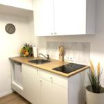 Küche mit weißen Schränken, Holzplatte, Spüle und Induktionskochfeld.