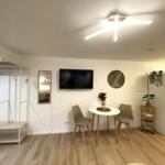 Wohnraum mit Esstisch, TV und Kleiderschrank. Holzfußboden und weiße Wände.