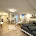 Schlafzimmer mit Bett, Sessel und Küchenbereich im Hintergrund.