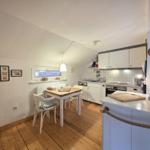 Kitchen with dining table, white cabinets, and wooden floor. Window with view of wall.