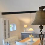 Vintage bell in foreground, dining room with table and chairs in background.