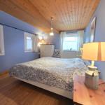 Bedroom with wooden floor, blue walls, and wooden ceiling. Bed, nightstand, and dresser are present.