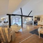 Living and dining area with wooden floor and black beams. Furniture including chairs and sofa.