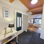 Entrance area with table, lamp, and view into living room with wooden floor and ceiling beams.