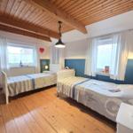 Two beds with white frames and striped bedding. Wooden ceiling and floor. Windows with white curtains.
