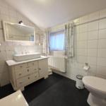 Bathroom with sink, mirror, toilet, and window.
