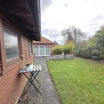Backyard with lawn, plants, and patio area beside wooden house wall.