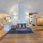 Living area with fireplace, wooden floor, and kitchen area in background.