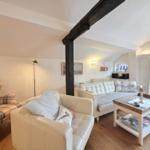 Living room with sofa, armchair, and wooden table. Visible beams and window.