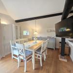 Dining room with wooden floor, white table and chairs, TV and balcony access.