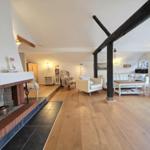 Living room with fireplace, wooden floor, and heavy beams. Furniture is light and modern.