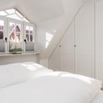 Schlafzimmer mit weißem Bett, Fenster und Kleiderschrank.