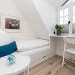 Schlafzimmer mit Bett, Schreibtisch und Fenster. Holzboden und weiße Wände.