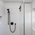 Dusche mit schwarzen Armaturen und Glaswand. Fenster mit Jalousie.