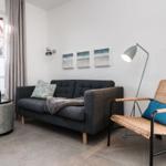 Ein Wohnzimmer mit grauem Sofa, Stuhl und Fenster. Auf Tisch steht eine Flasche.