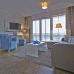 Wohnbereich mit Sofa, Sessel und Balkon. Schlafzimmer im Hintergrund.