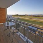 Terrasse mit Tisch und Stühlen, Blick auf Grünfläche und Wasser.