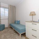 Schlafzimmer mit blauer Couch, Schrank und Fenster mit Vorhängen.