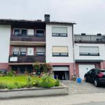 Zweistöckiges Haus mit Balkonen, Garage und Garten. Ein Auto parkt vor dem Haus.