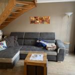 Wohnzimmer mit grauem Sofa, Holztisch und Holztreppe.