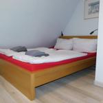 Ein Bett mit weißer Bettwäsche und rotem Matratzenbezug in einem Zimmer mit Holzboden.