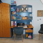 Schreibtisch mit Stuhl, Regal und Kleiderschrank in einem Kinderzimmer.