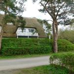 Haus mit Strohdach, weißer Veranda und grüner Hecke