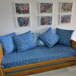 Ein Sofa mit blauen Kissen und einem Holzrahmen. An der Wand hängen sechs gerahmte Fotos.