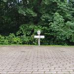 Pflasterweg führt zu einem Holzschild mit der Nummer 06 vor grüner Vegetation.
